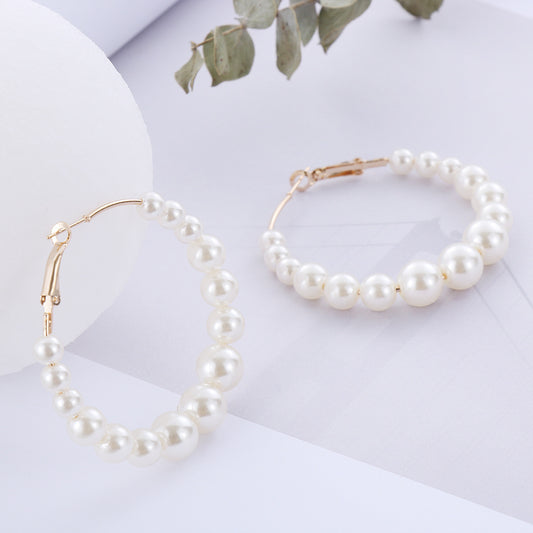 Pearl necklace and bracelet on a white surface with green leaves in the background