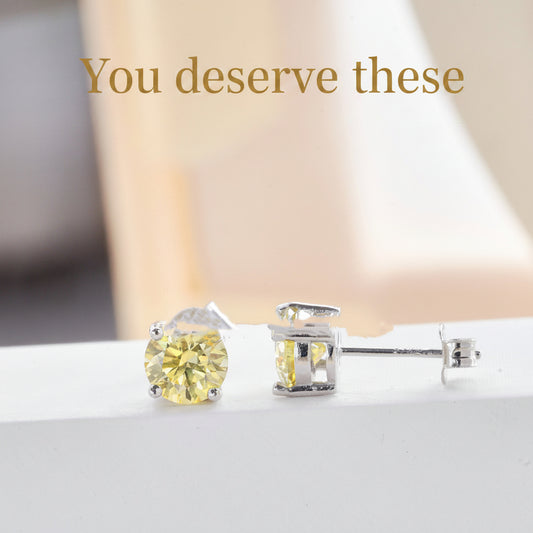 Pair of yellow gemstone stud earrings on a white surface with a soft blurred background