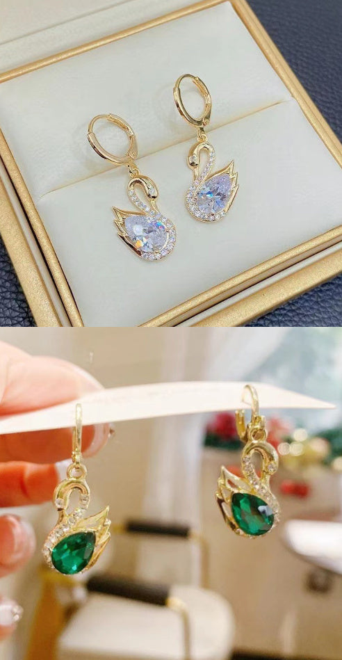 Gold earrings with gemstones displayed in a box and held by a hand.