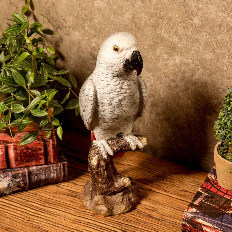 White parrot figurine on a branch with plants in the background