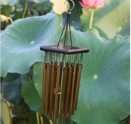 Bronze wind chime hanging against a green leafy background