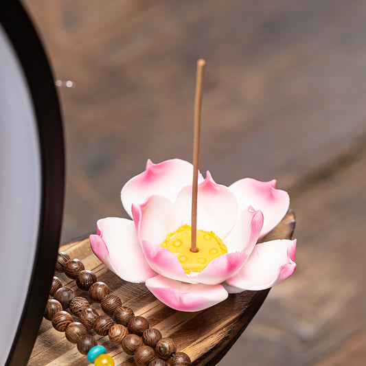 Lotus-shaped incense holder with a stick of incense on a wooden surface