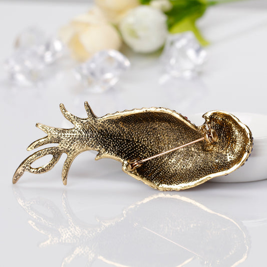 Gold fish-shaped brooch on a white surface with flowers in the background