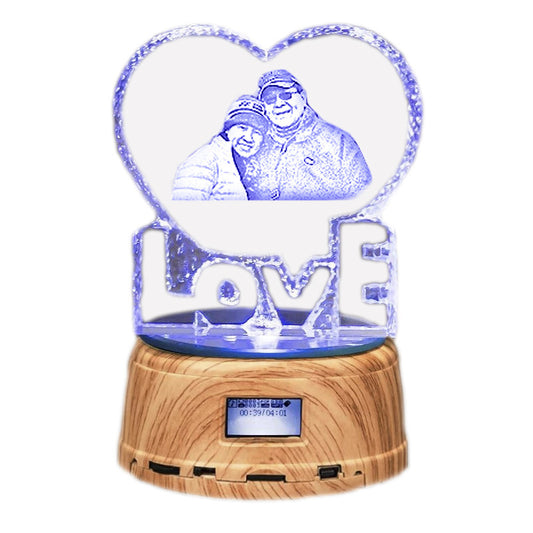 Heart-shaped crystal ball with a wooden base displaying a photo of two people and the word 'LOVE'.