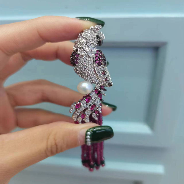 Hand holding a decorative pink brooch with gemstones and pearls against a light blue background