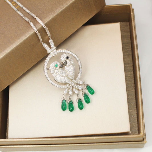 Elegant necklace with a bird design and green gemstones in a brown box.
