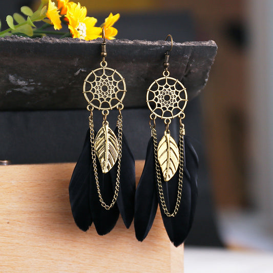 Gold and black feather earrings on a wooden surface with blurred background