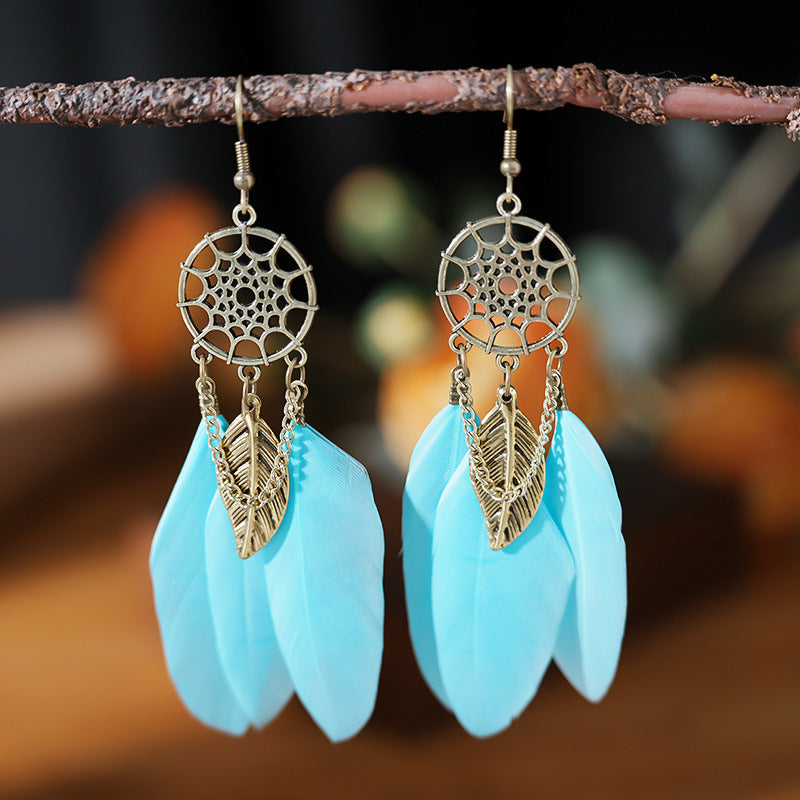 Blue feather earrings with gold accents hanging on a branch against a blurred natural background.