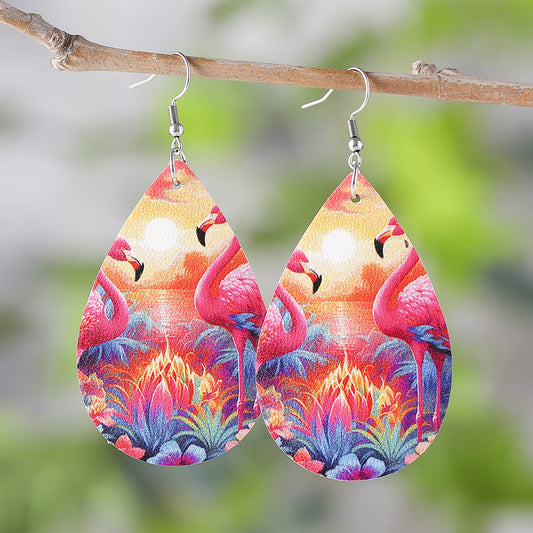 Teardrop-shaped earrings with flamingo design hanging on a branch with a blurred green background.