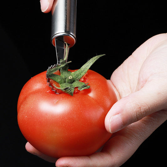 Hand using a tomato corer to remove the core from a tomato against a black background