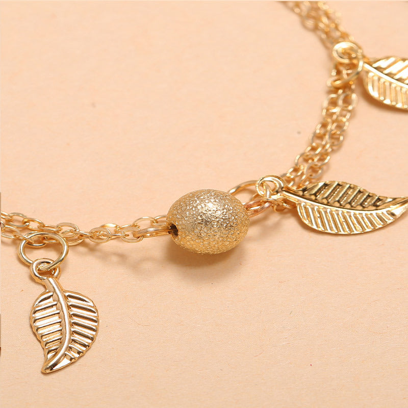 Gold bracelet with leaf charms on a beige background