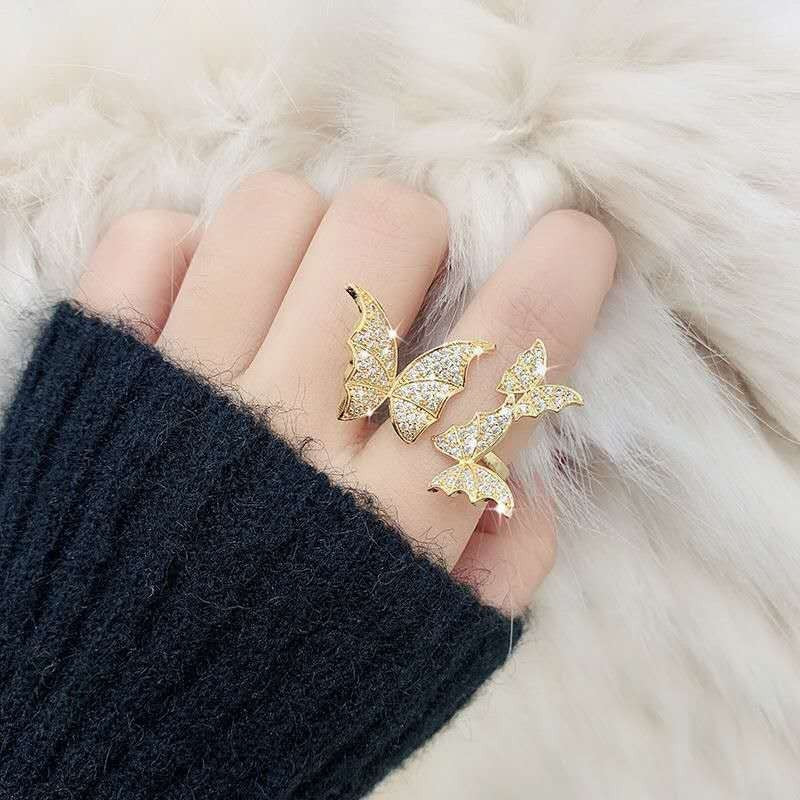 Gold butterfly rings on a hand with a black fingerless glove against a fur background