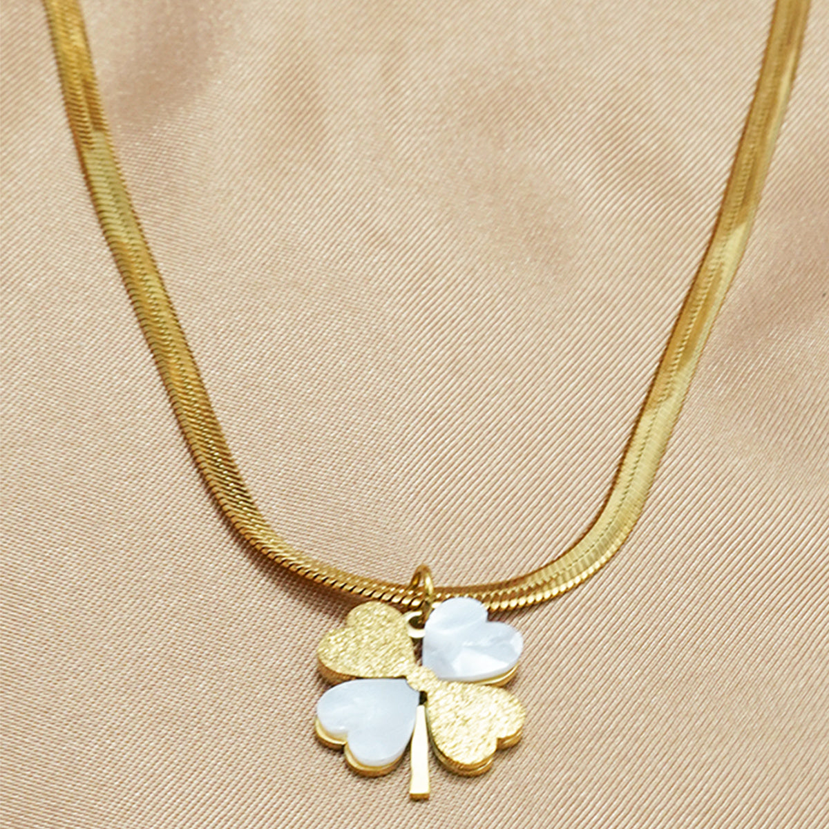 Gold necklace with a four-leaf clover pendant on a beige fabric background