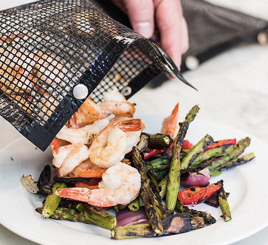 Grilled shrimp and vegetables on a plate with a mesh bag.
