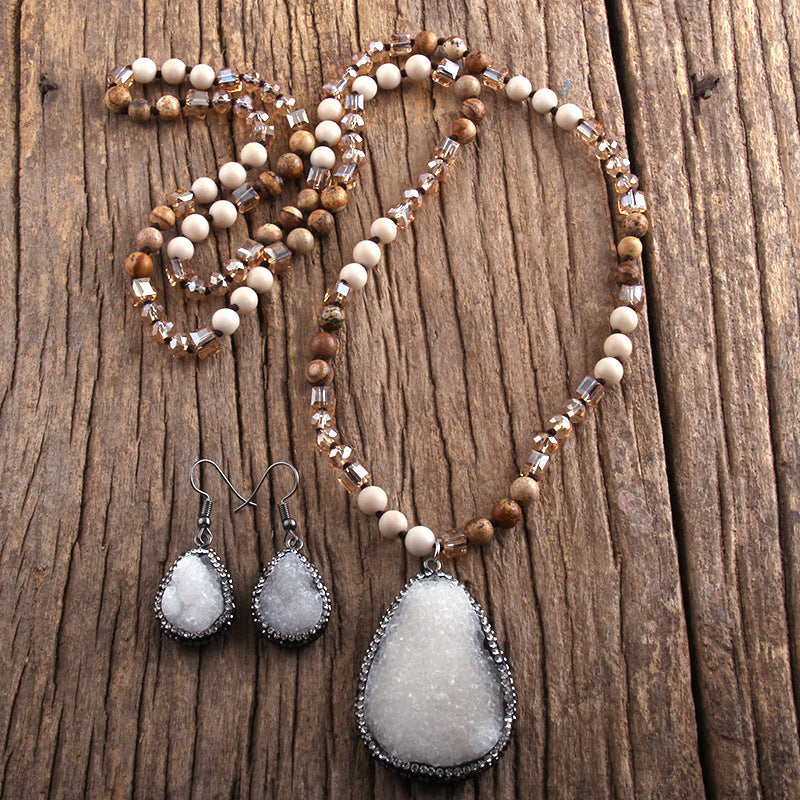 Beaded necklace with gray pendant and matching earrings on a wooden surface