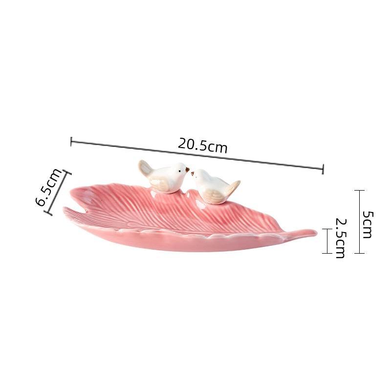 Pink ceramic leaf-shaped dish with two bird figures and measurements on a white background