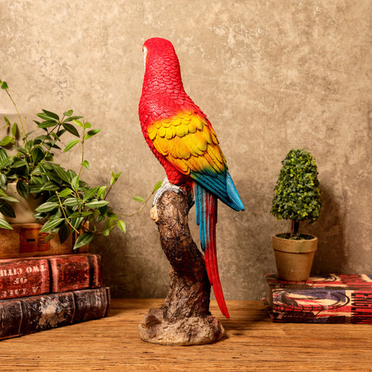 Colorful parrot statue on a branch with decorative books and plants in the background