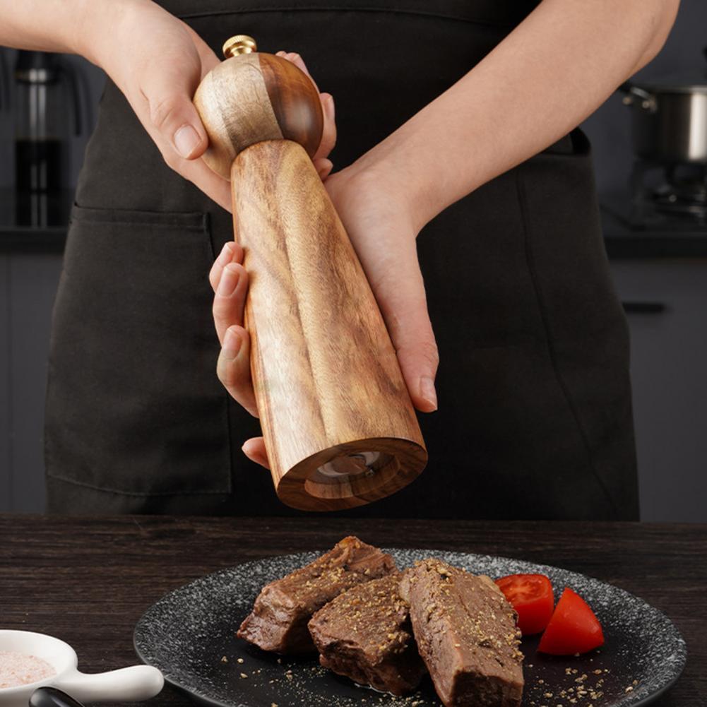 Wooden pepper grinder being used over a plate of food in a kitchen setting