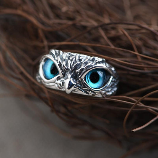 Silver owl-shaped ring with blue eyes on a textured brown surface