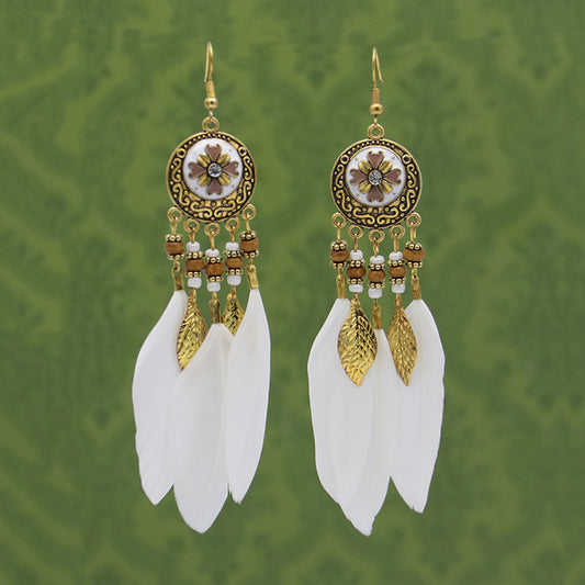 Pair of gold and white feathered earrings on a green patterned background