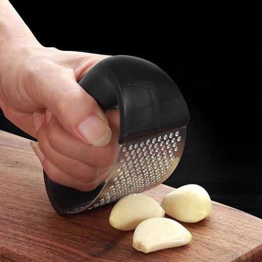 Hand using a garlic press on a wooden cutting board with garlic cloves.