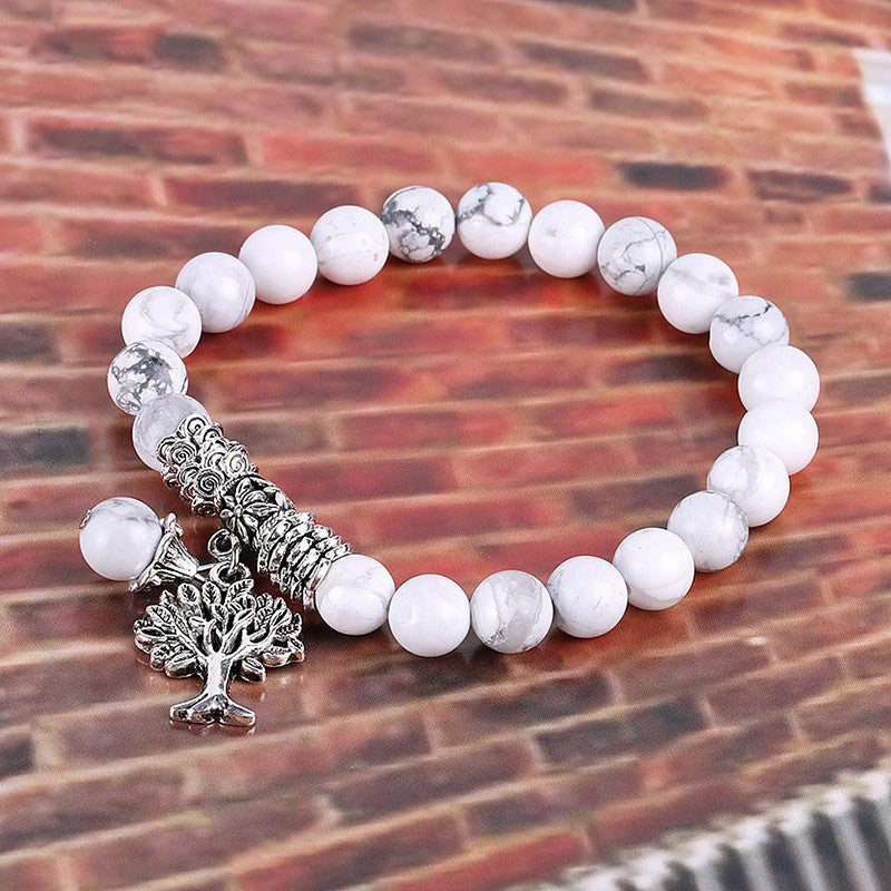 White beaded bracelet with a silver tree charm on a brick background
