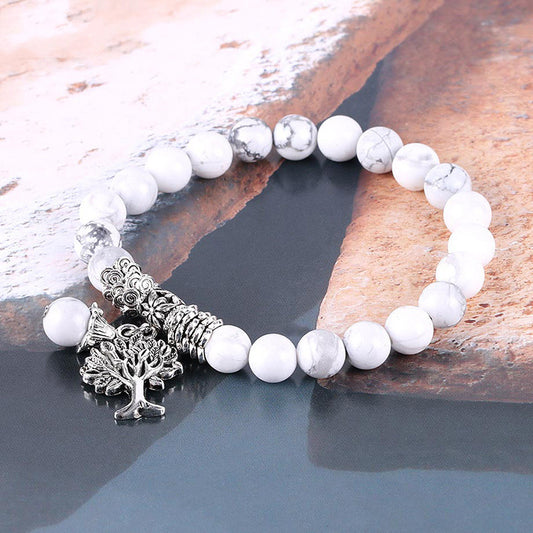 White beaded bracelet with silver tree charm on a stone surface