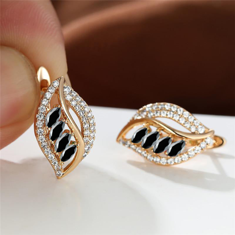 Gold earrings with blue gemstones held by a hand on a white surface.