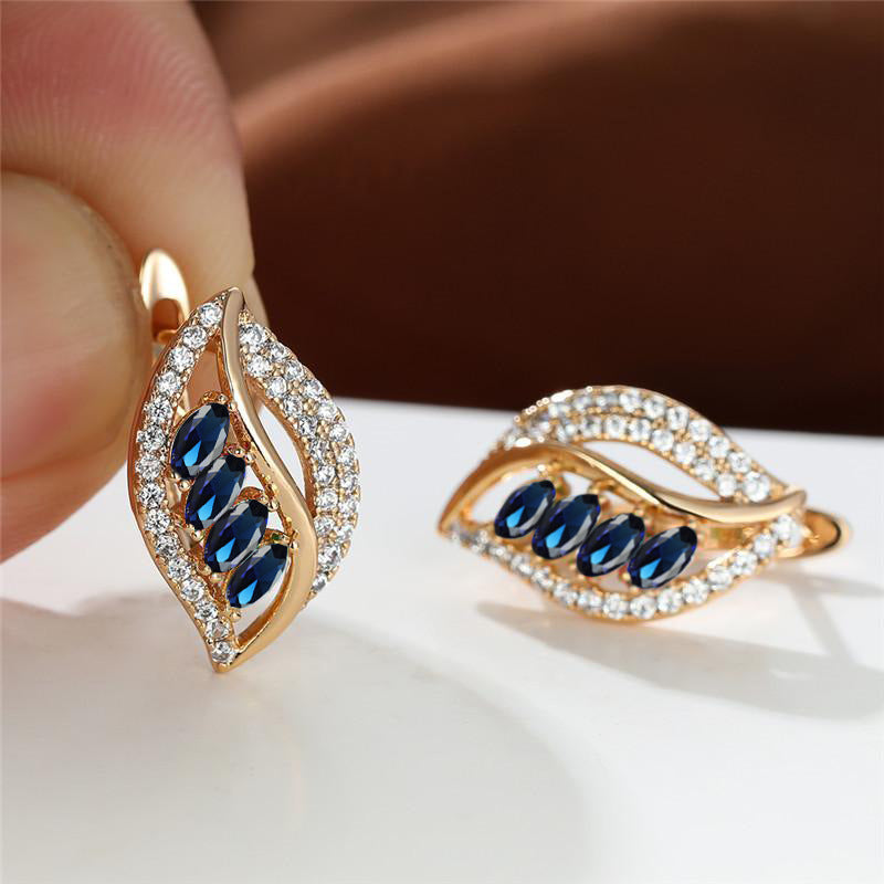 Gold earrings with blue gemstones held by a hand on a white surface.