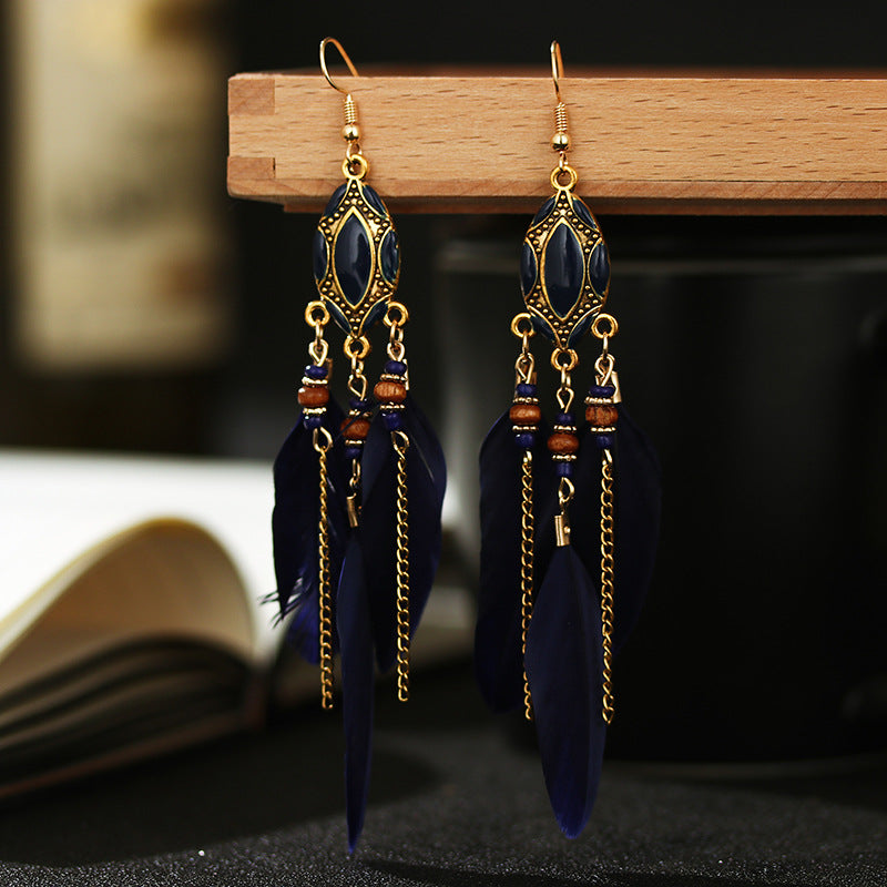 Pair of blue feather earrings with gold accents on a wooden stand from Nested Wisdom