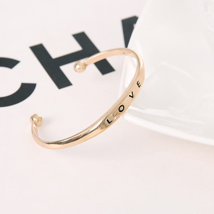 Gold bracelet with 'LOVE' engraving on a white background