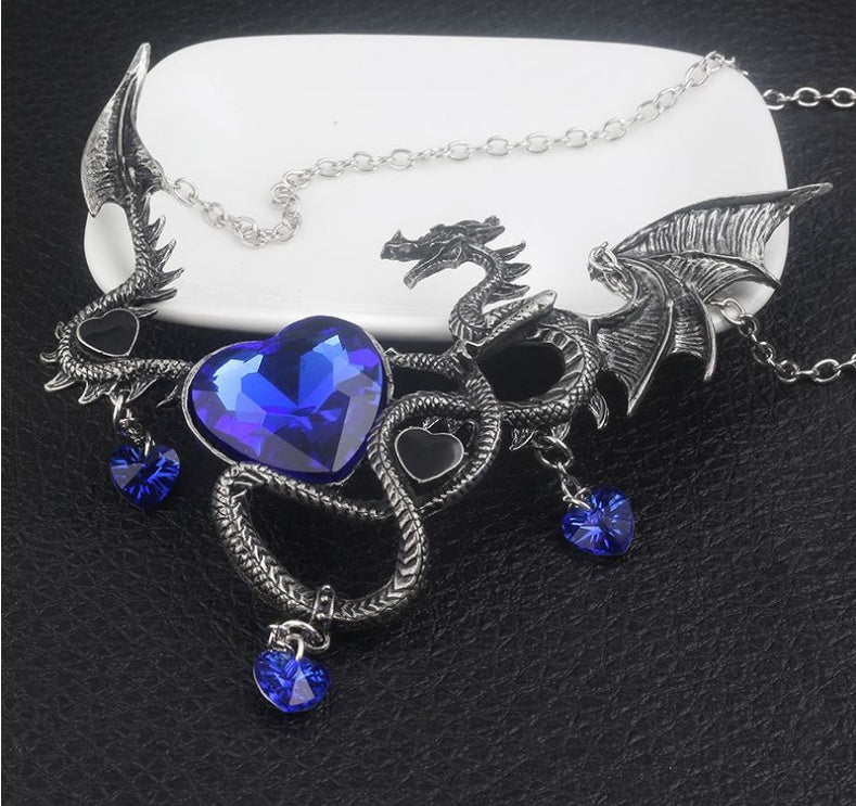 Dragon-shaped necklace with blue heart pendant on a black surface