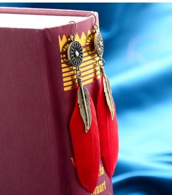 Red feather earrings with gold accents on a red book against a blue watercolor background