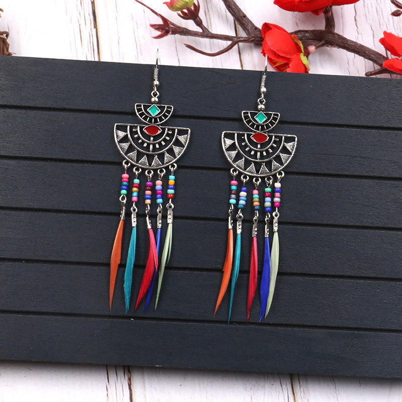 Colorful feather earrings with decorative elements on a dark wooden surface.