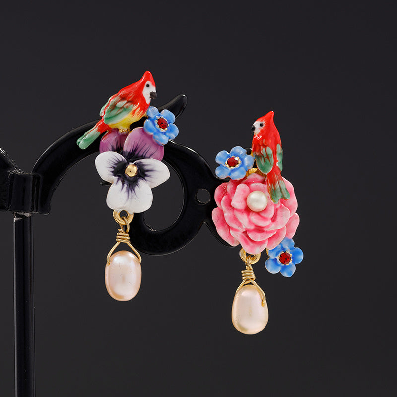 Colorful parrot and floral earrings on a black stand with a dark background
