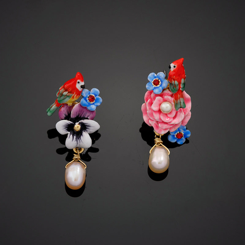Pair of earrings with birds, flowers, and pearls on a dark background