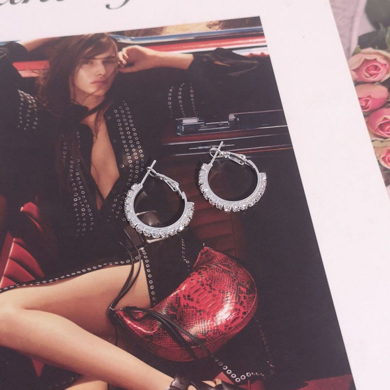 Silver hoop earrings on a magazine with a model and red handbag in the background