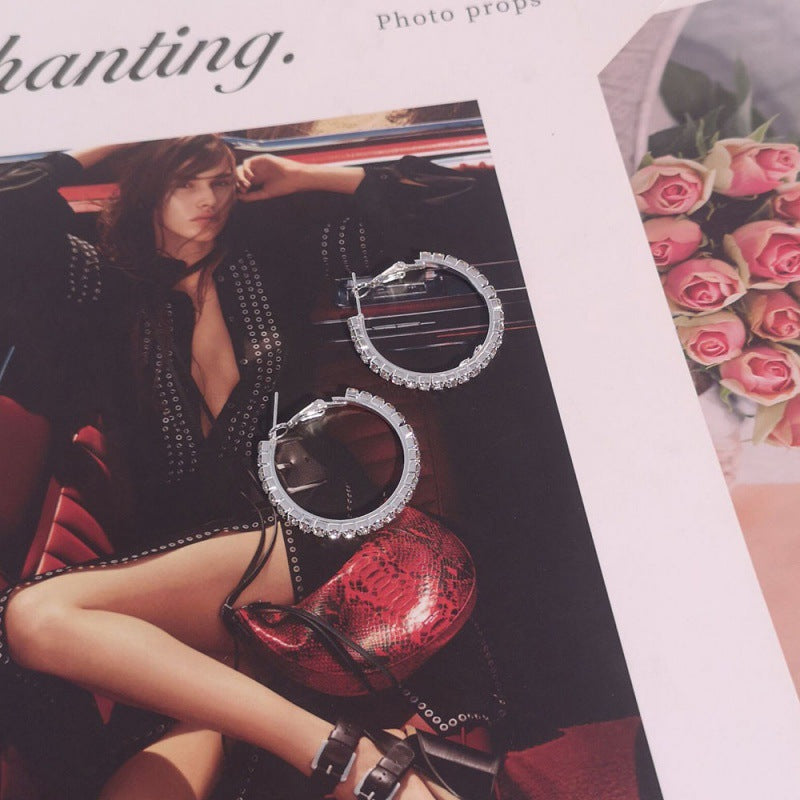 Silver hoop earrings on a magazine with a model and flowers in the background