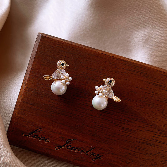 Pair of bird-shaped earrings with pearls on a wooden jewelry box labeled 'Love Jewelry'.