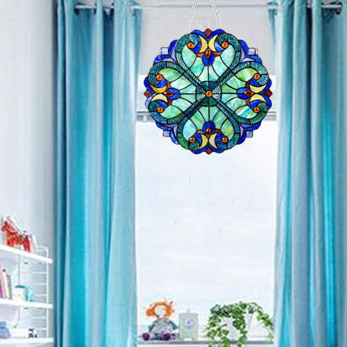 Decorative stained glass window hanging in front of a window with blue curtains.