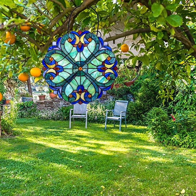 Decorative stained glass butterfly hanging in a garden with green grass and trees.