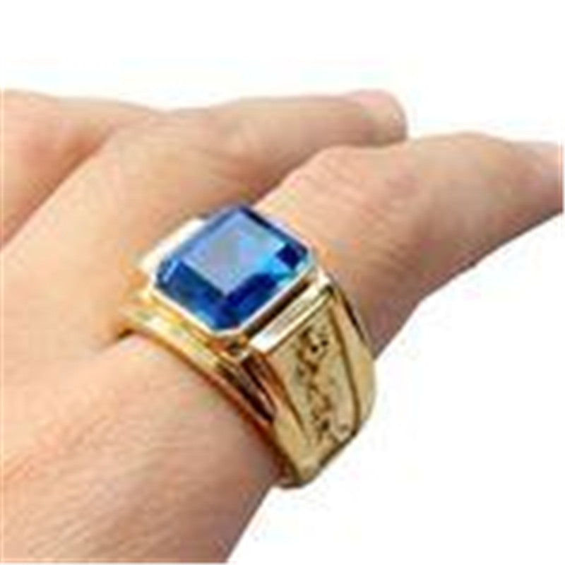 Gold ring with a blue gemstone on a finger against a white background