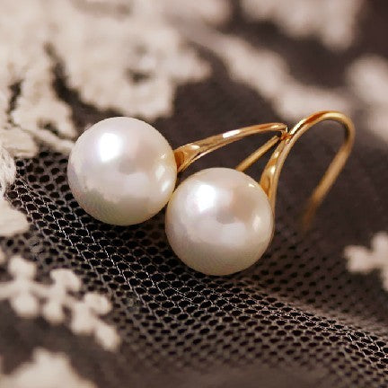 Pearl earrings with gold hooks on a textured surface