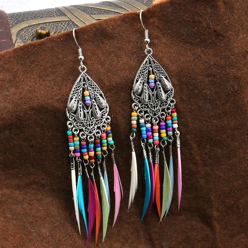 Colorful feather earrings with intricate silver designs on a brown textured background