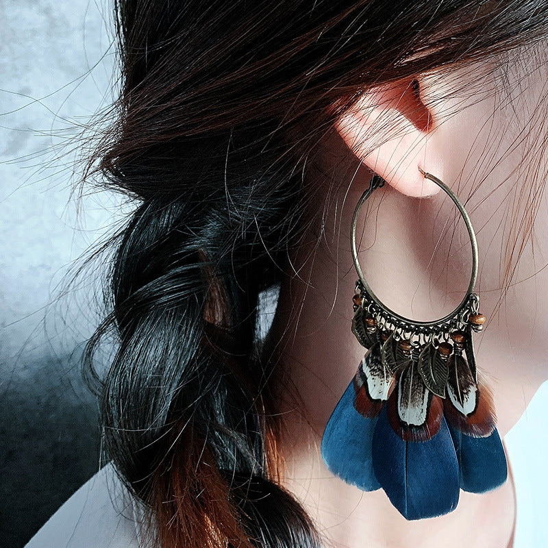 Close-up of an ear wearing a decorative hoop earring with blue tassels.