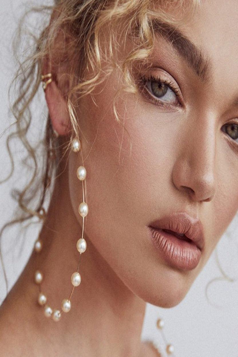 Close-up of a woman wearing pearl earrings with a neutral background