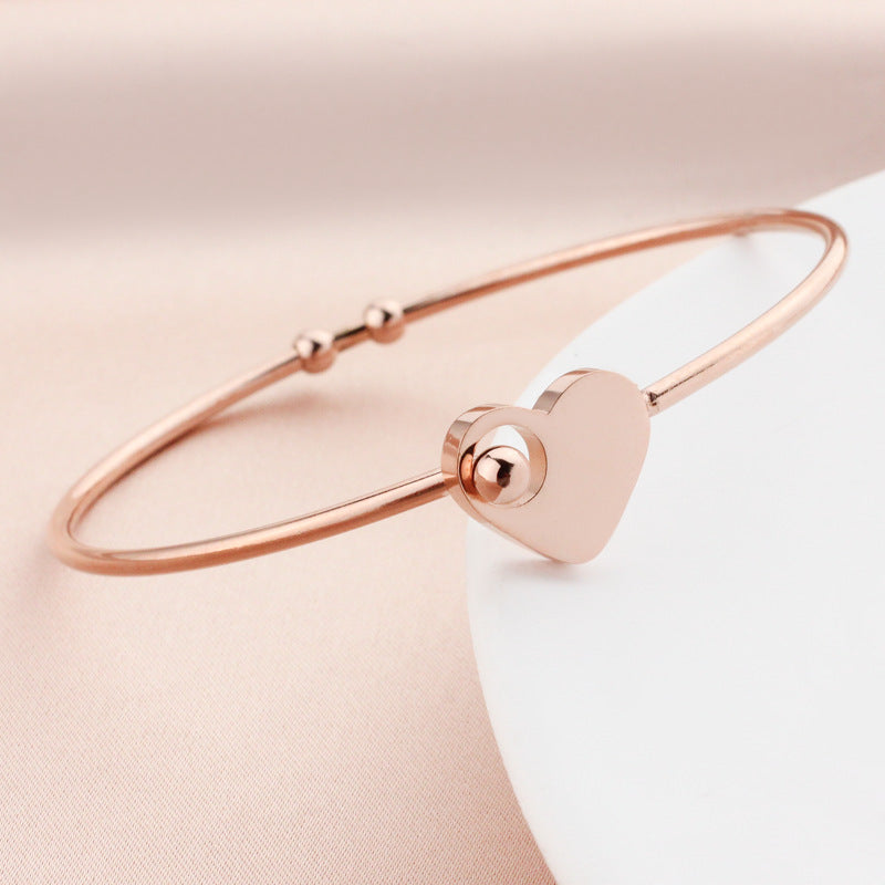Rose gold bracelet with a heart-shaped clasp on a soft pink background