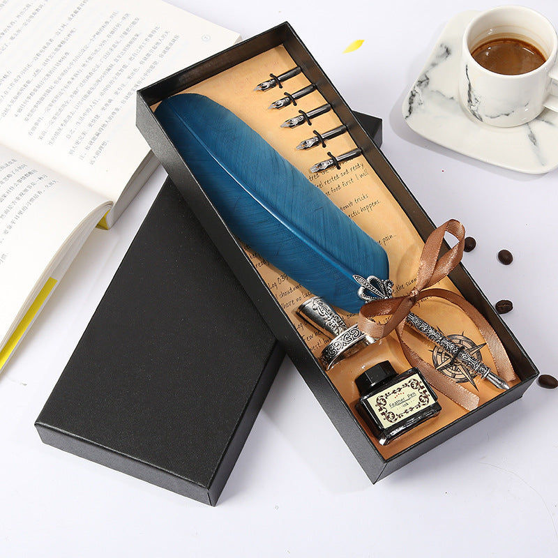 Fountain pen set with blue feather, ink bottle, and nibs in a black box on a white surface.