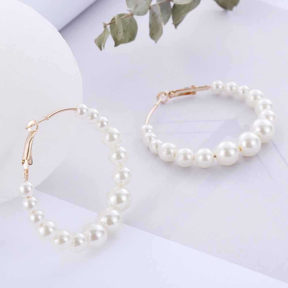 Pearl necklace and bracelet on a white surface with green leaves in the background