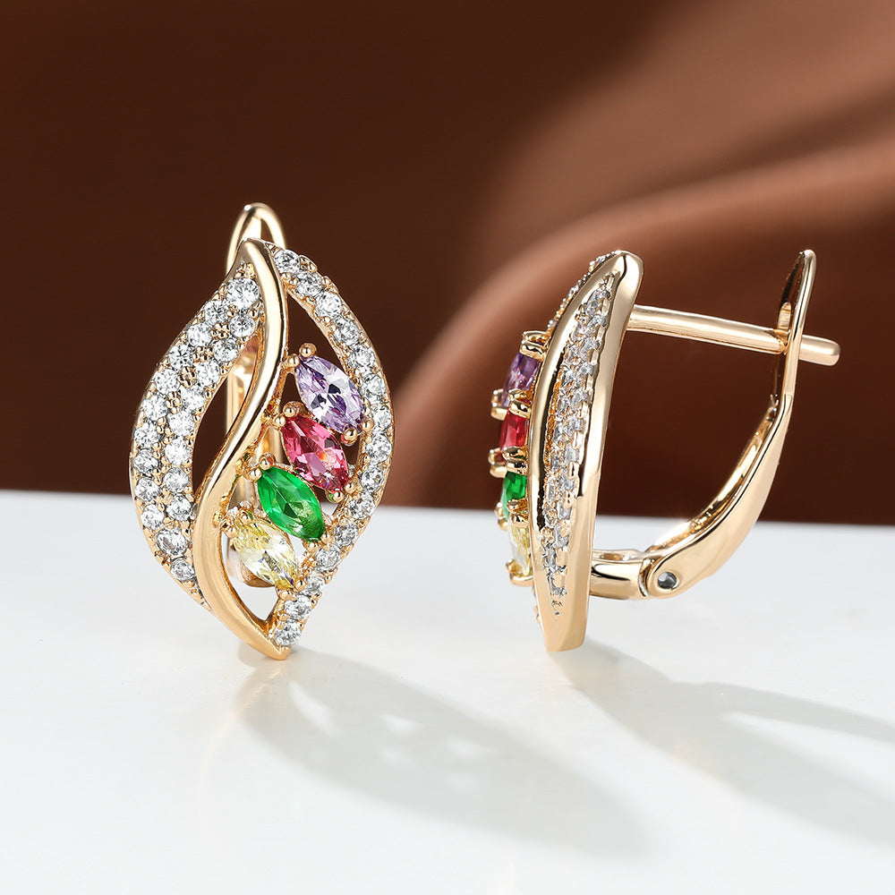 Gold earrings with colorful gemstones on a white surface with a brown background